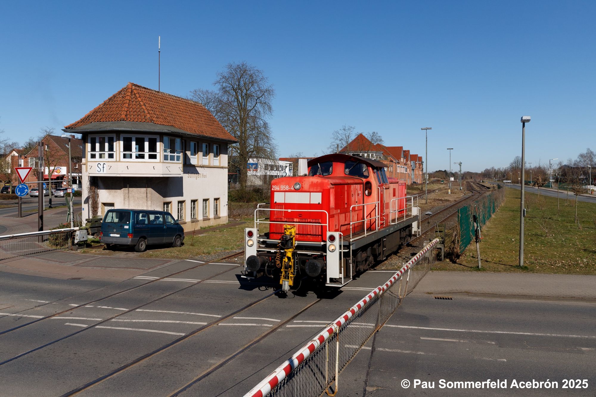 Diesellok 294 958 der DB Cargo AG in verkehrsrot fährt aus dem Bahnhof Sulingen aus und passiert dabei das Stellwerk Sulingen Fahrdienstleiter (Sf) und den Bahnübergang Nienburger Straße