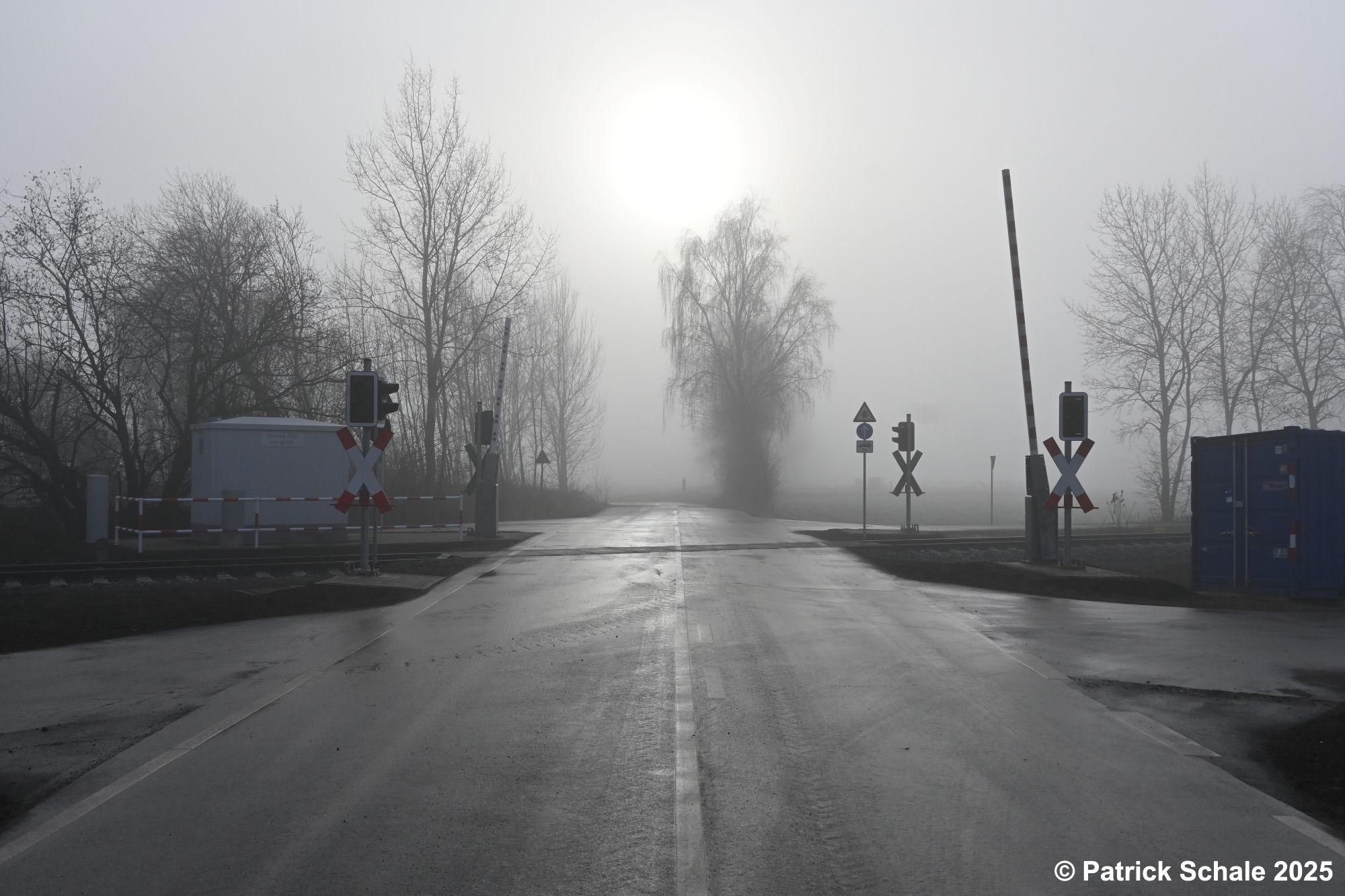 Erneuerter Bahnübergang mit neuen Lichtzeichenanlagen, Halbschranken und neuem Schalthäuschen am Birkenkampsweg an einem nebeligen Dezembertag aufgenommen mit Gegenlicht