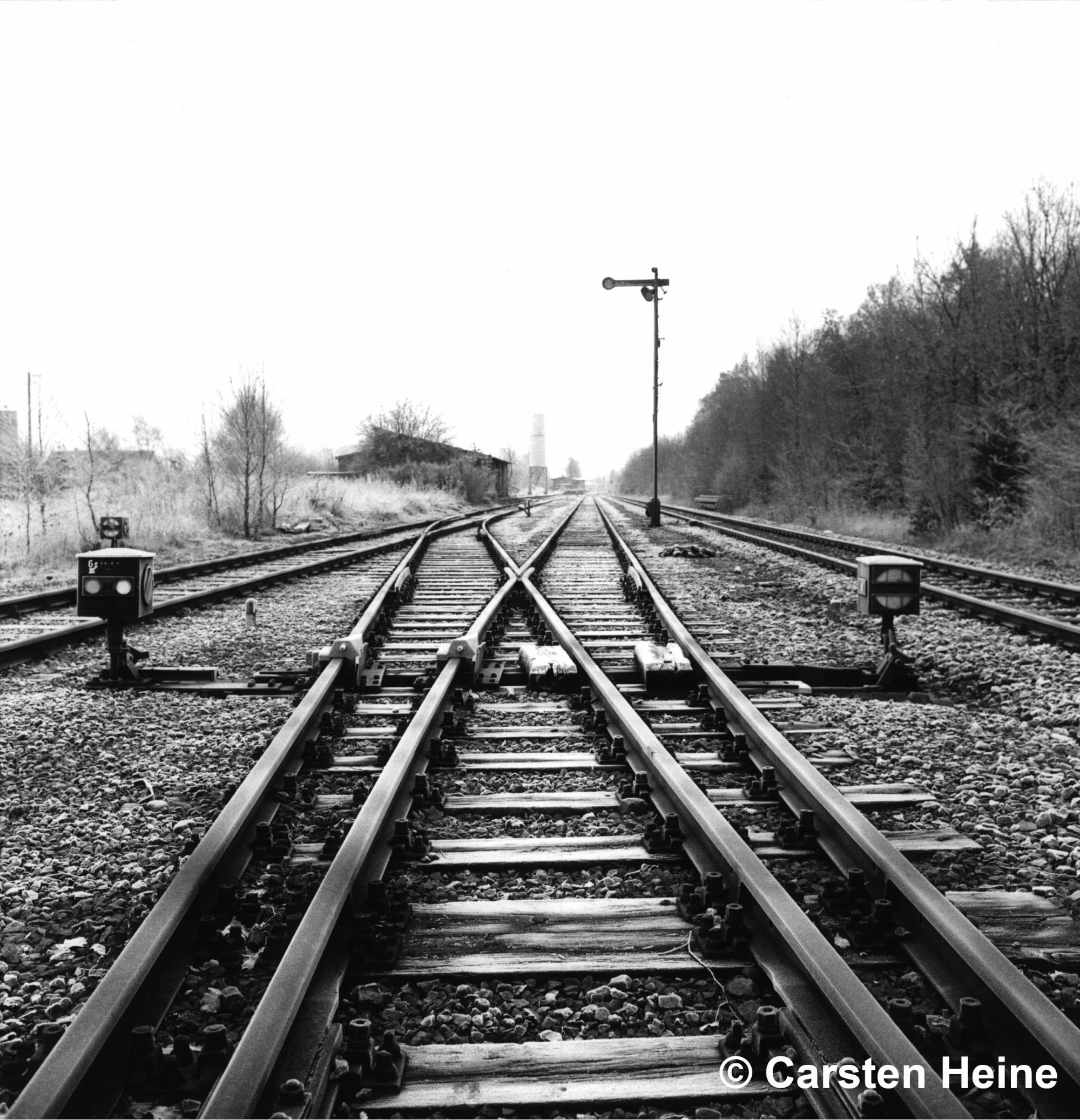Blick in den Bahnhof Schwaförden mit einem Ausfahrsignal am Hauptgleis, links davon die Nebengleise gesichert durch Gleissperren, im Hintergrund das Empfangsgebäude/Güterschuppen