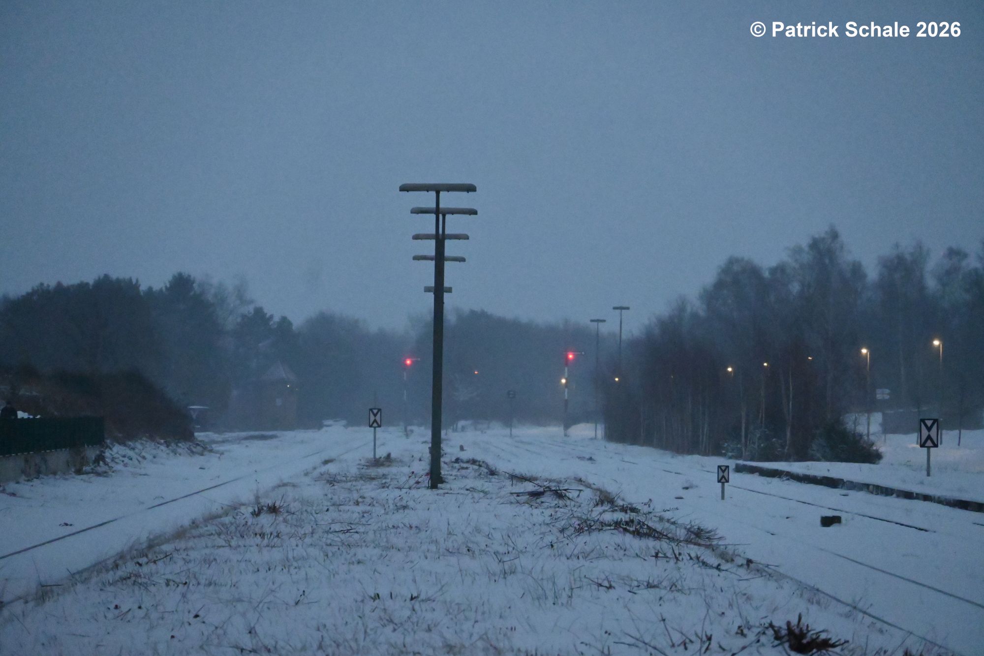 Blick vom Bahnsteig in Richtung Norden auf Vorsignaltafeln, Bahnsteiglampen und im Hintergrund die rot leuchtenden Zielsignale