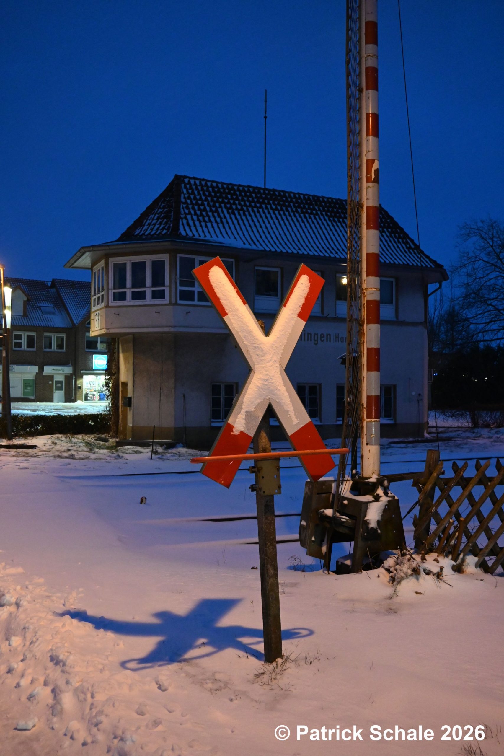 Eingeschneites Andreaskreuz mit Schattenwurf in den Schnee am Bahnübergang Nienburger Straße, im Hintergrund Stellwerk Sf