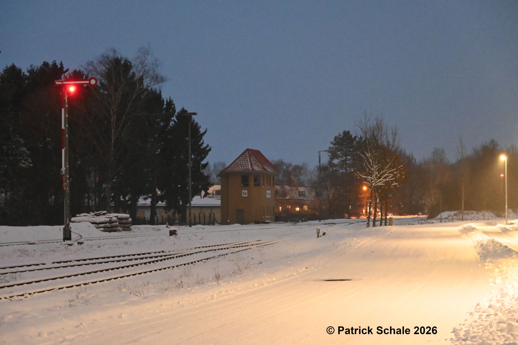 Blick auf das Stellwerk Sn im Schnee, links ein Zielsignal in Stellung Halt, HP 0, rechts eine Straßenlaterne