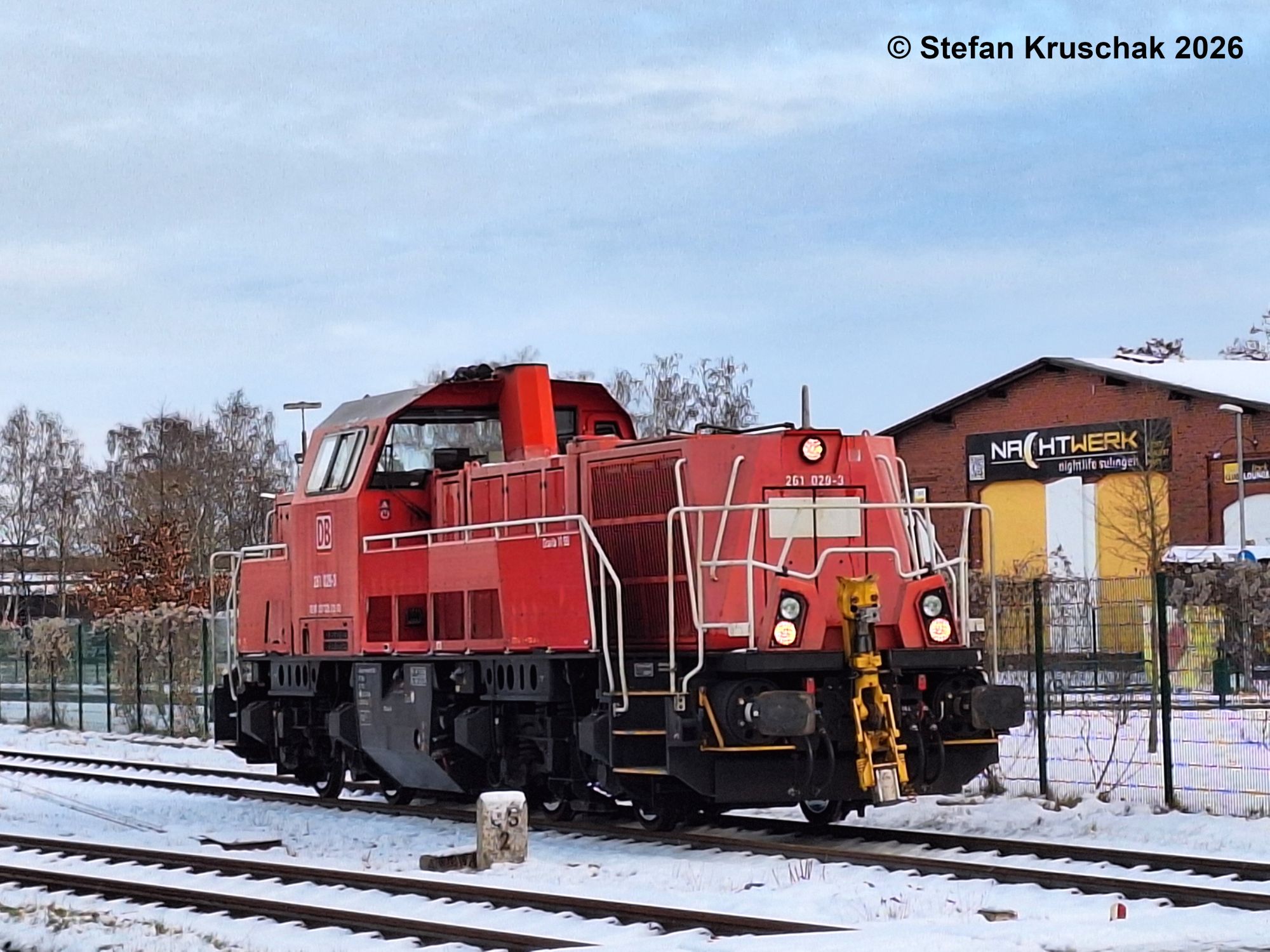 Diesellokomotive 261 029-3 der DB Cargo AG in verkehrsrot im verschneiten Bahnhof Sulingen; Im Hintergrund ist der ehemalige Lokomotivschuppen zu sehen, in dem zuletzt die Diskothek Nachtwerk ansässig war.