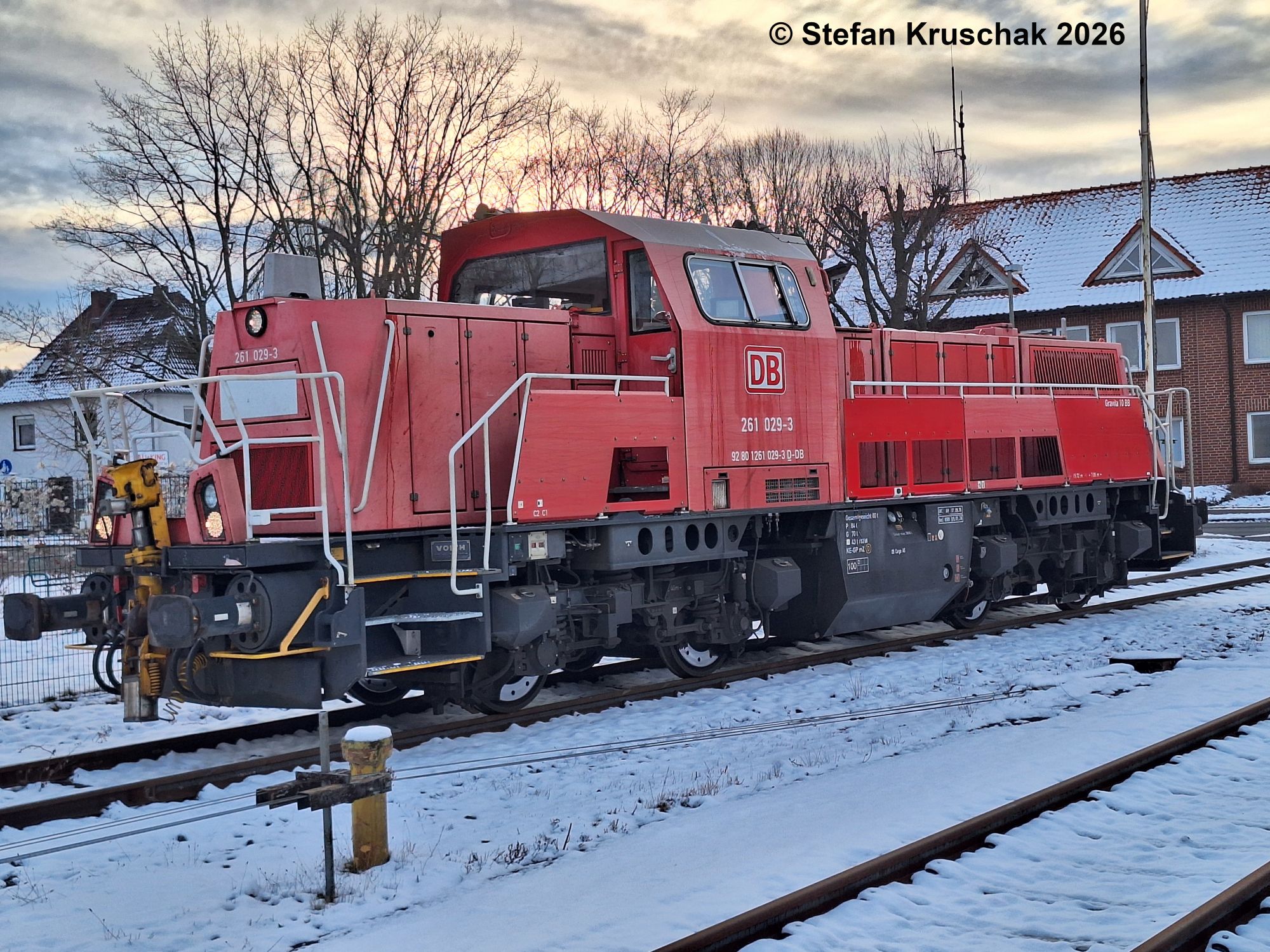 Diesellokomotive 261 029-3 der DB Cargo AG in verkehrsrot steht vor dem Bahnübergang Nienburger Straße im verschneiten Bahnhof Sulingen