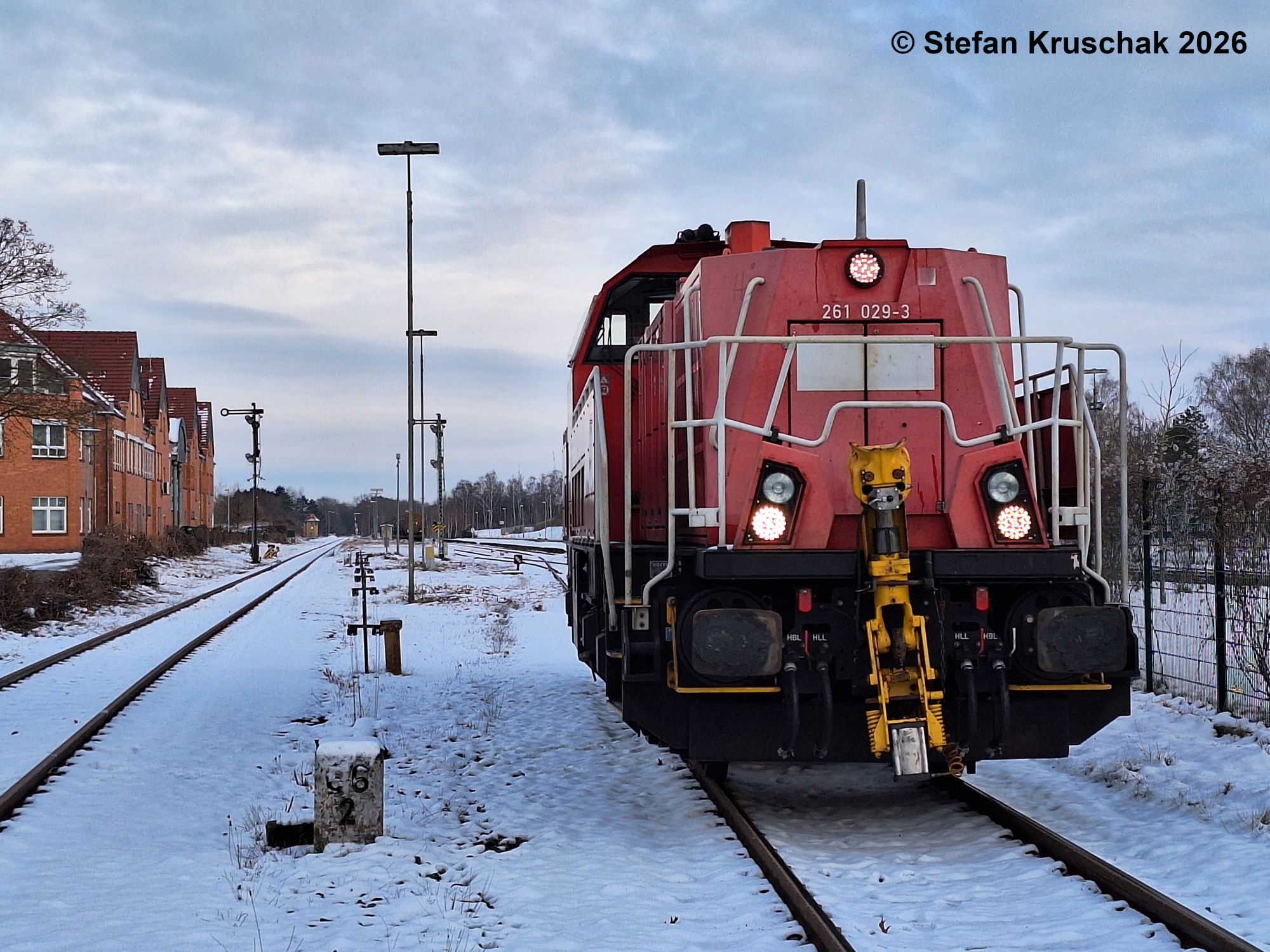 Verkehrsrote Diesellokomotive 261 029-3 der DB Cargo AG im verschneiten Bahnhof Sulingen, links neben der Lokomotive der Kilometerstein 66,2, im Hintergrund die 2 Ausfahrsignale