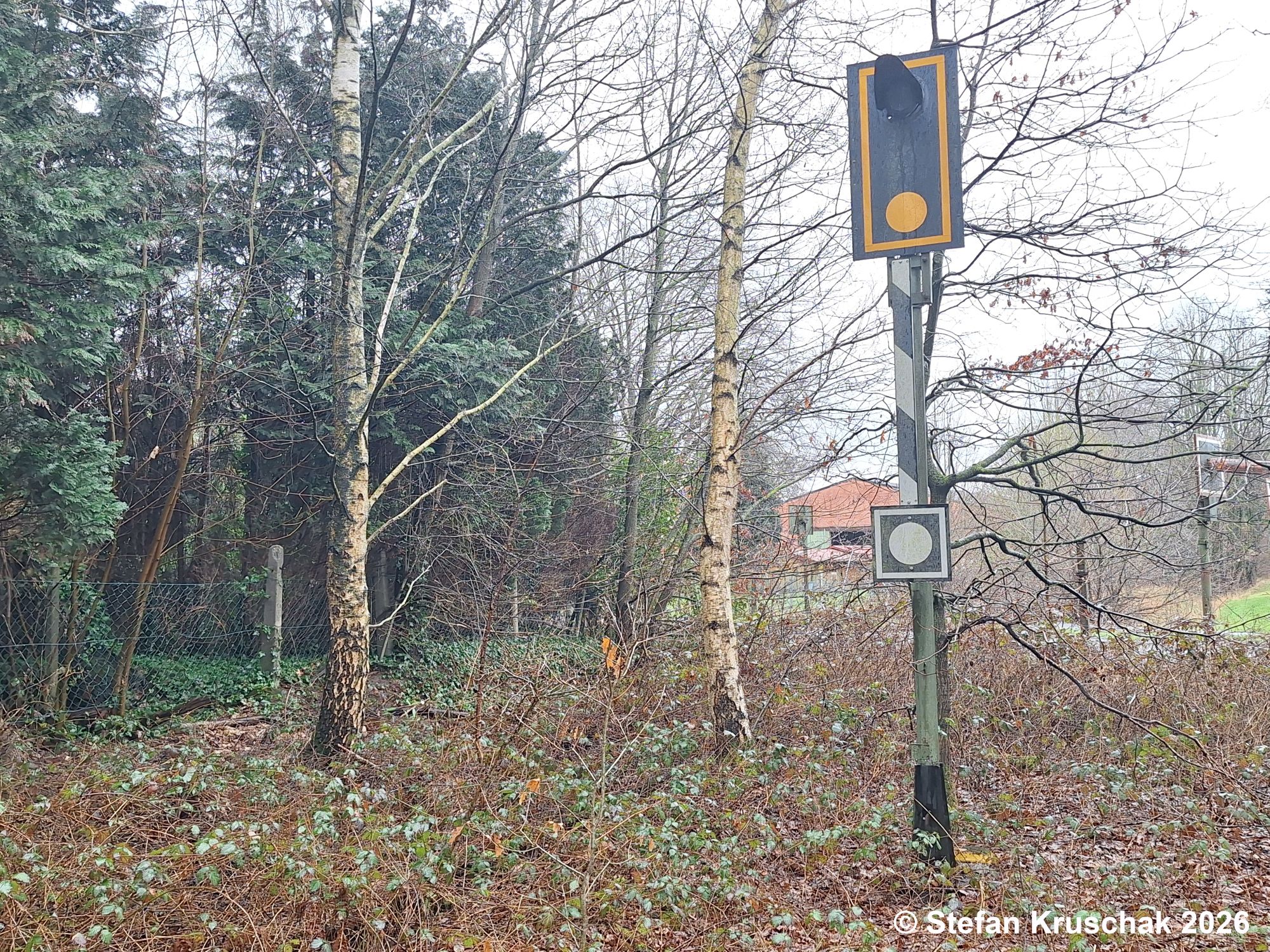 Bahnübergangüberwachungssignal als Wiederholer an der zugewachsenen Strecke in Schwaförden, im Hintergrund der dazugehörige Bahnübergang mit Blinklichtern