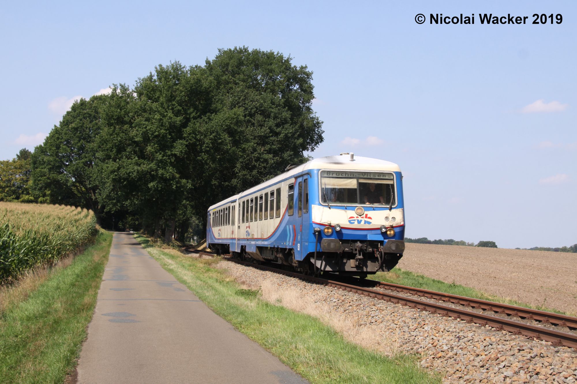 Triebwagen der Baureihe 628 der evb auf dem Weg nach Bruchhausen-Vilsen zwischen Ackerland, einer Straße und Bäumen