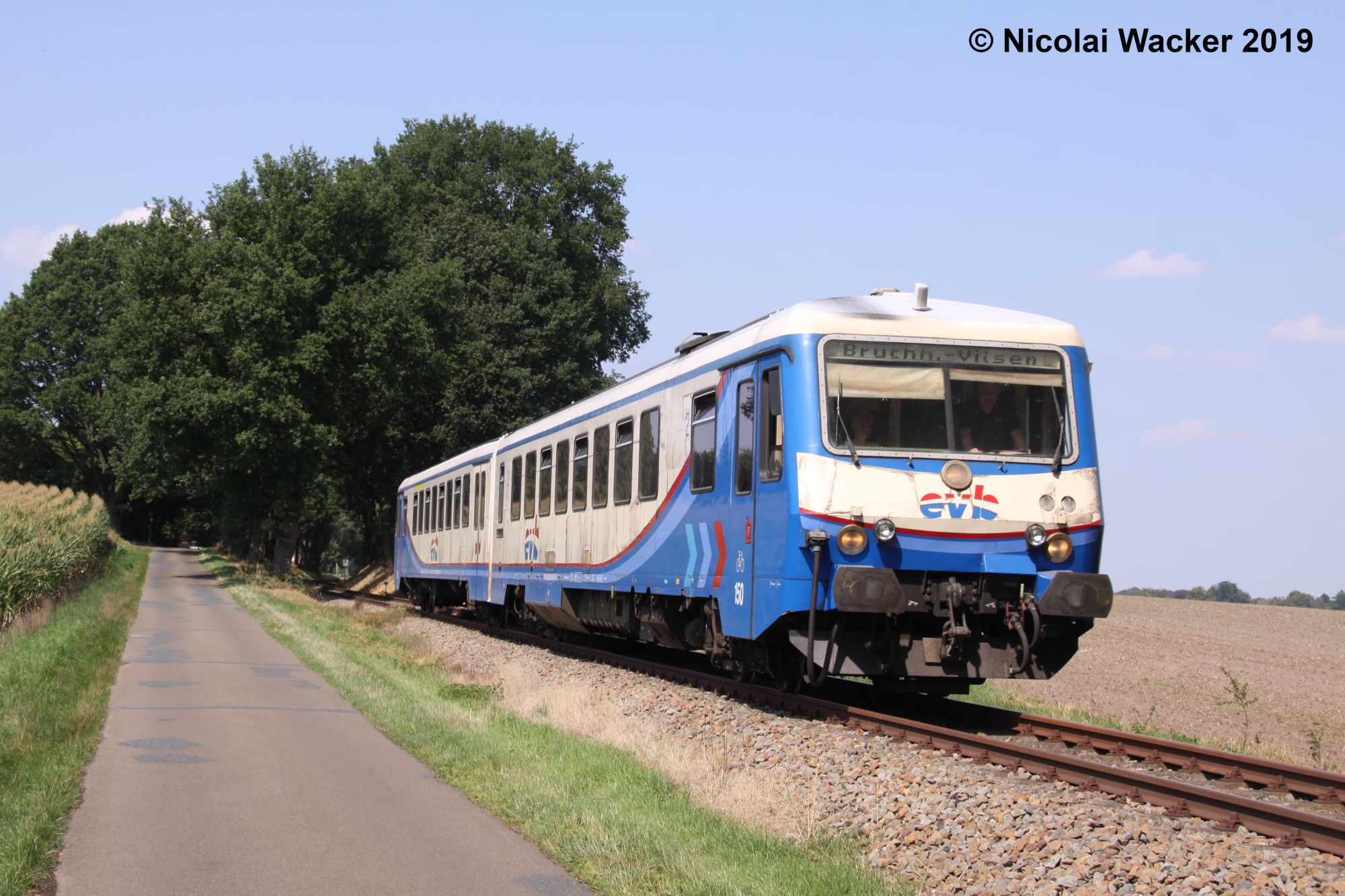 Triebwagen der Baureihe 628 der evb auf dem Weg nach Bruchhausen-Vilsen zwischen Ackerland, einer Straße und Bäumen
