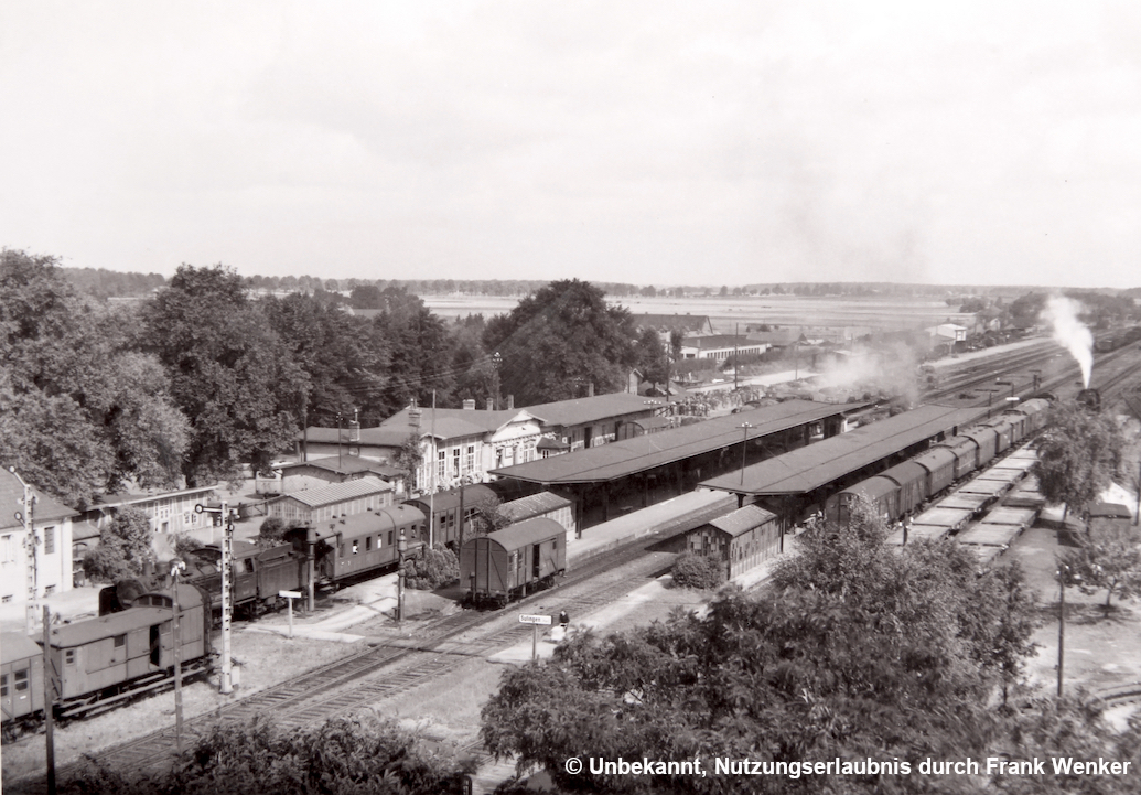 Blick auf den Sulinger Bahnhof mit dem Empfangsgebäude mit Güterabfertigung, einem Personenzug mit Ausfahrt auf HP 2, Langsamfahrt, Ausfahrsignalen, zwei überdachten Bahnsteigen und diverse Güterwagen (von links nach rechts)