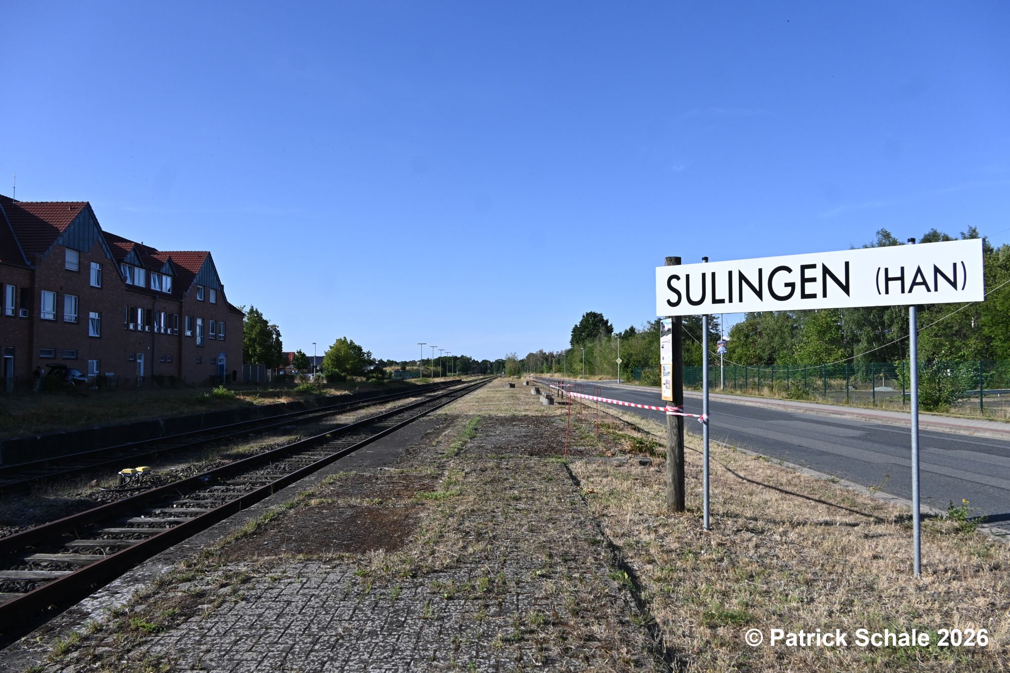 Frisch gemähter Bahnsteig an Gleis 4 im Bahnhof Sulingen mit Absperrband zur Straße und Fahrplan am Holzmasten hinter dem Stationsschild