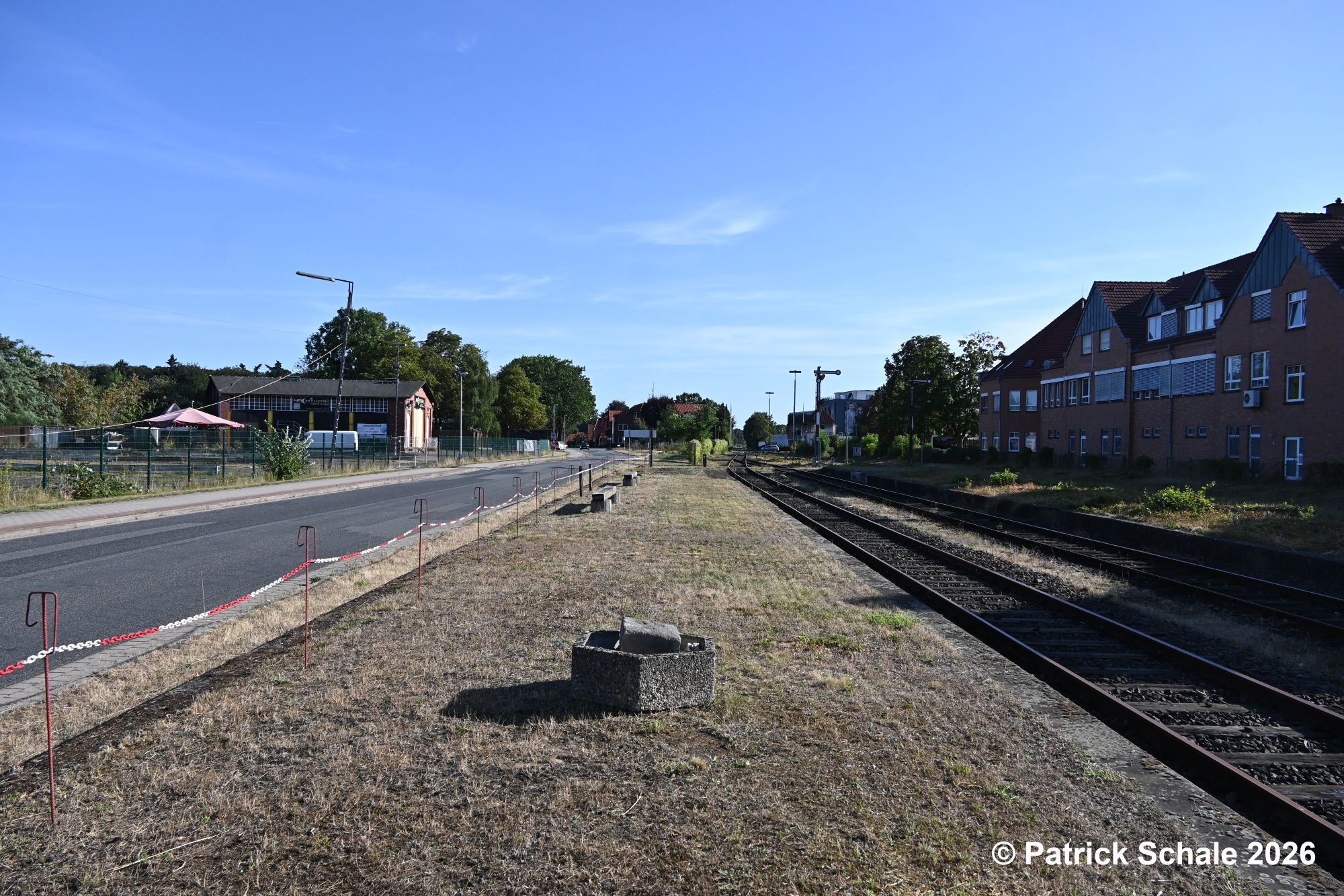 Frisch gemähter Bahnsteig an Gleis 4 im Bahnhof Sulingen mit Absperrkette zur Straße; im Hintergrund links der ehemalige Lokomotivschuppen
