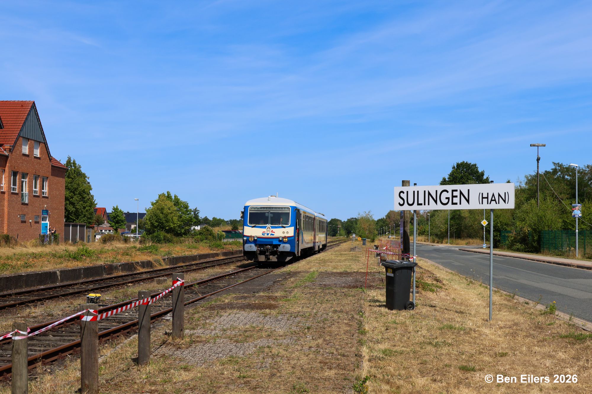 Triebwagen der evb steht zur Fahrt nach Diepholz bereit, links Wohn- und Geschäftshaus, rechts Stationsschild