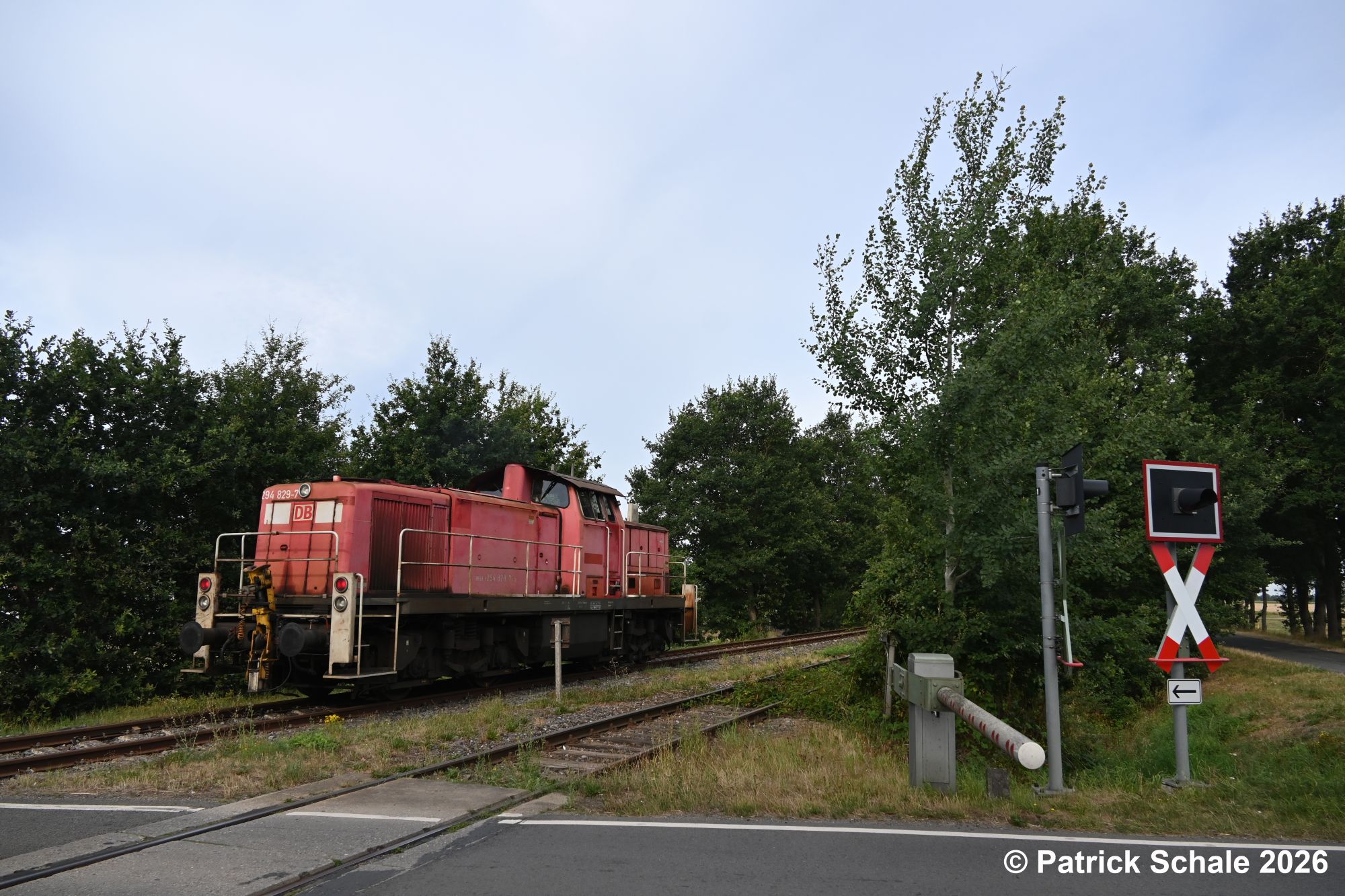 Diesellokomotive der Baureihe 294 hat den Bahnübergang Dickeler Straße in Rehden-Wetschen passiert und fährt weiter Richtung Diepholz. Im Vordergrund liegt das Anschlussgleis zu BTR-Logistik.